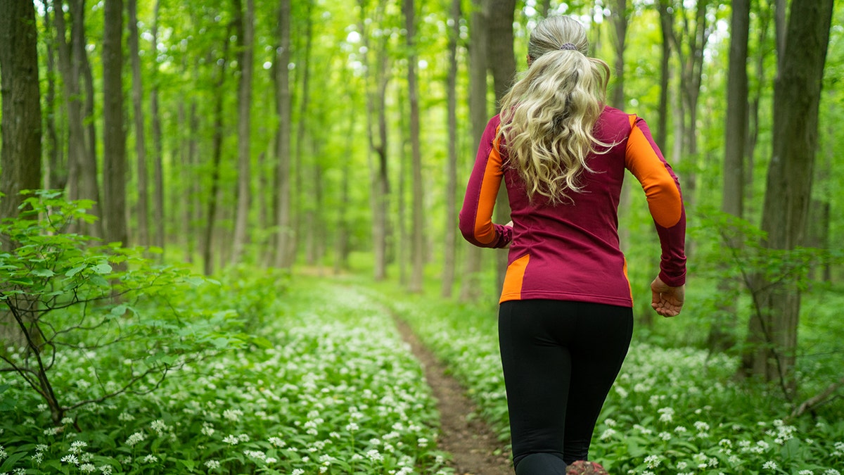 Woman jogging through lush vegetation in a forest.