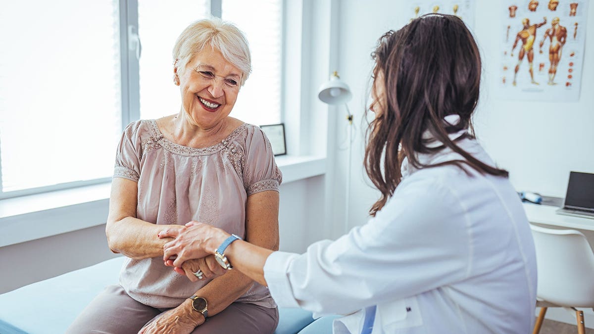 Doctor reassures female patient with hand gesture during treatment discussion.