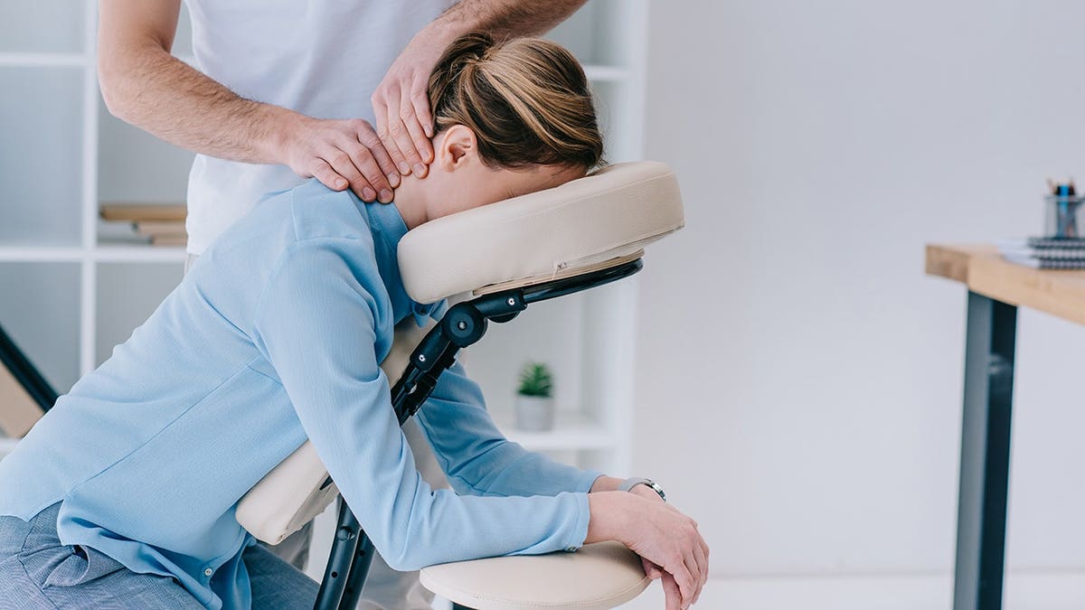 Masseur performing seated neck massage on a businesswoman.