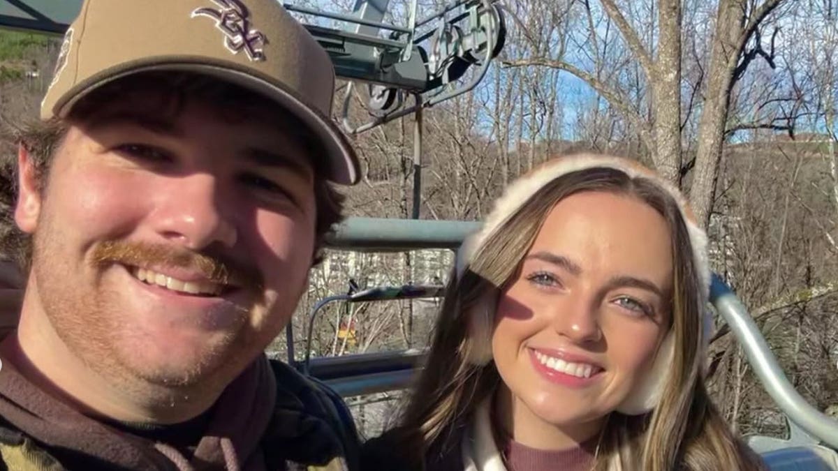 Shane Hirstius and his fiancée, Leah Fonte, smile for an outdoor selfie, with Hirstius wearing a baseball cap and Fonte wearing white earmuffs.