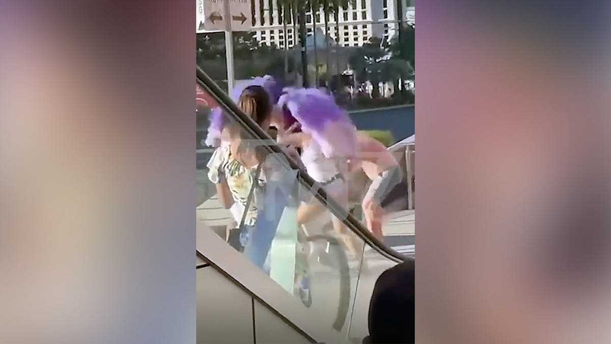 A shirtless man faces a woman wearing a purple feathered showgirl costume and white boots during a confrontation on the Las Vegas Strip.