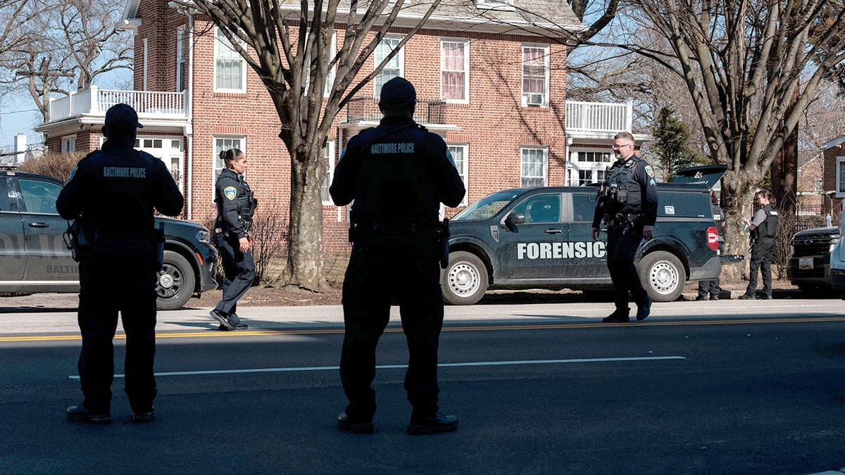 Baltimore Police officers standing and working near a marked scene of a shooting.