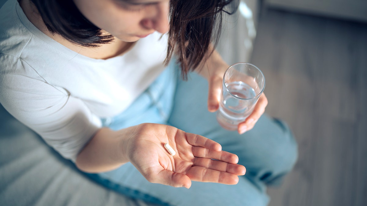 A woman about to take some pills, she is holding a glass of water