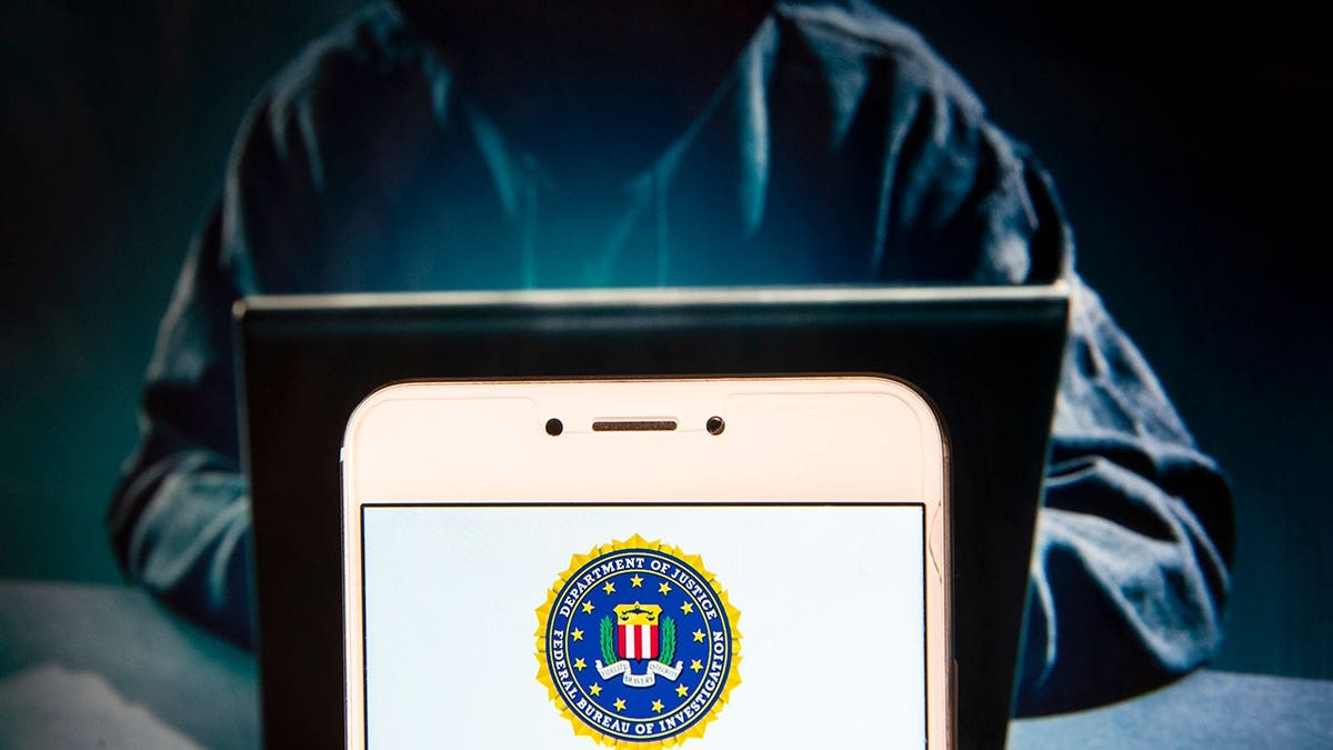 FBI logo displayed on an Android mobile device with a hacker figure in the background.