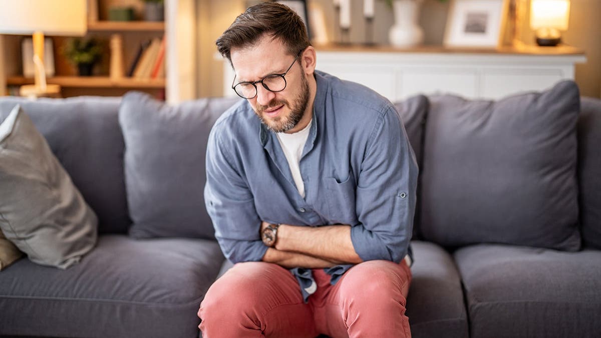 Man sits on couch holding his abdomen.