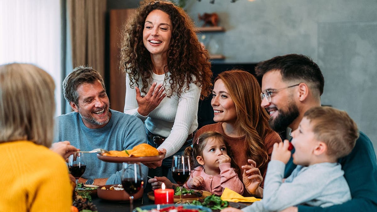 Multi-generation family seated around a dining table sharing a Thanksgiving meal with roast turkey.