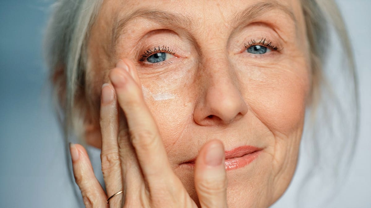 Senior woman applying under-eye face cream to her face.