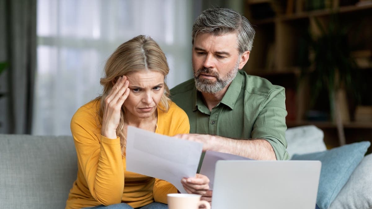 Stressed middle-aged couple reviewing financial papers and loan documents at home.