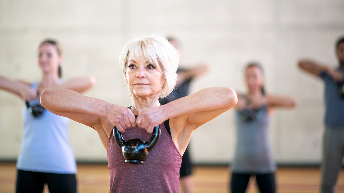 A fit senior woman is carrying a dumbbell in her fitness class.